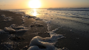 A beach with the sun setting over the horizon, creating a calm and serene atmosphere. - 6p Luxury apartment with panoramic roof terrace (Burgerbrug)