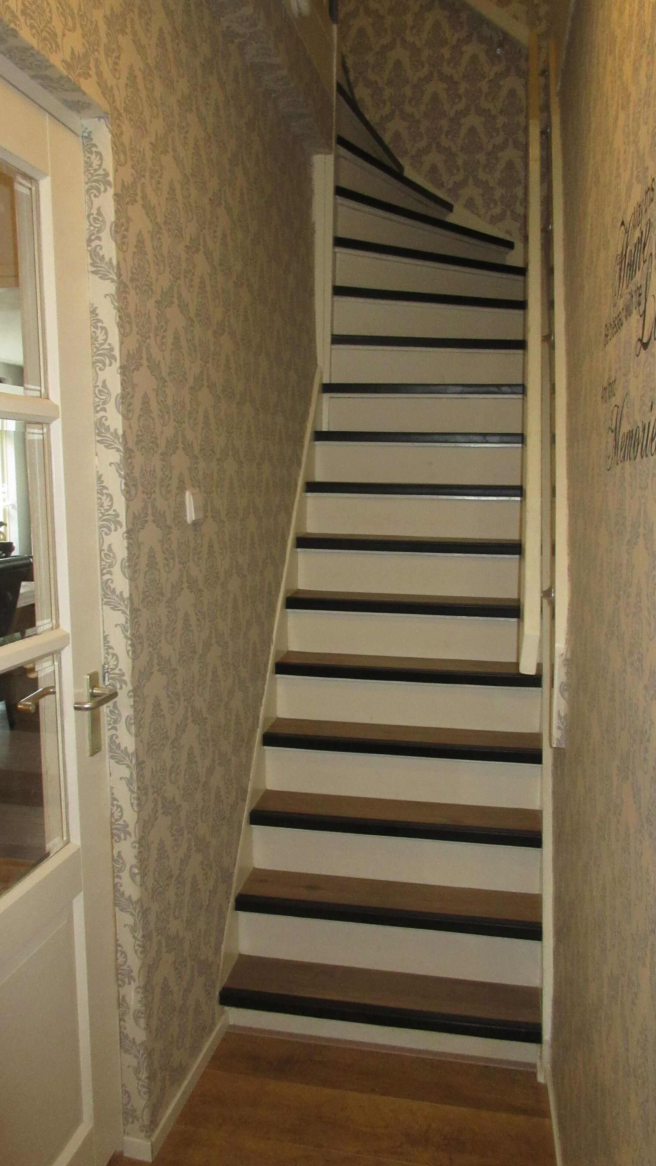A staircase with a wooden finish and a patterned wallpaper on the walls.