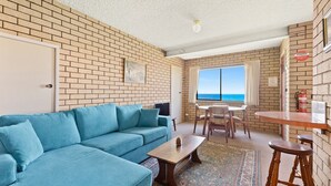 A room with a blue sofa, a wooden table, and a view of the sea through a window. - 1/15 Dalmeny Drive, Kianga (Kianga)