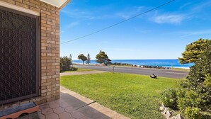 A coastal view from a porch with a brick wall, a grassy lawn, and a road leading to the beach. - 1/15 Dalmeny Drive, Kianga (Kianga)