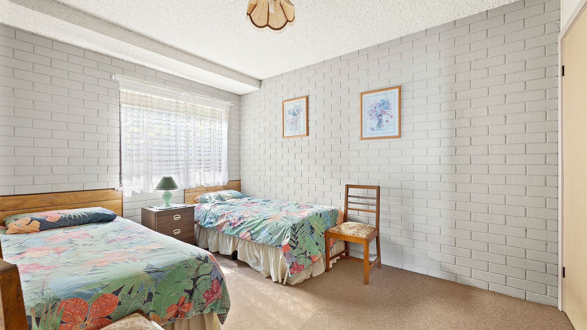 A bedroom with two beds, a chair, a nightstand, and a window with curtains.