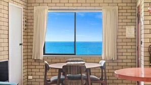 A room with a brick wall, a window with curtains, a round table, and two striped chairs. - 1/15 Dalmeny Drive, Kianga (Kianga)