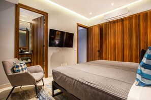 A bedroom with a bed, a chair, a television, and wooden paneling on the walls.