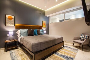 A modern bedroom with a bed, bedside tables, a chair, and artwork on the walls. - Chic 1BR in Romantic Zone w/pool (Puerto Vallarta)