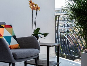 A balcony with a grey sofa, a colorful geometric pillow, a potted plant, and a view of buildings. - Chic 1BR in Romantic Zone w/pool (Puerto Vallarta)