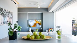 Un salon moderne doté d’un téléviseur à écran plat, d’un ventilateur de plafond et d’une table sur laquelle se trouvent une assiette de pommes vertes et une carafe en verre.