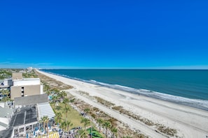 A beachside hotel with a view of the ocean, a parking area, and a building with a flat roof.
