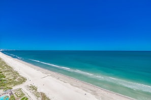 A beach with clear turquoise waters, a sandy shore, and a few people walking. - 💎Large Oceanfront~Lazy River~Awesome Amenities~ Caribbean Resort 1904💎 (Myrtle Beach)