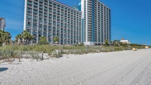Ein Hochhaus-Hotel mit mehreren Balkonen, direkt neben einem Sandstrand.