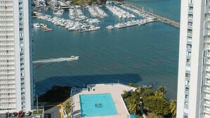 Un hotel moderno con vista a una marina con barcos, piscina y un paisaje montañoso.