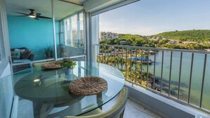 Un balcón con una mesa de vidrio, un ventilador de techo y vistas a un río y edificios.