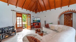 Una sala de estar con un sofá blanco, techo de madera, televisor y una estantería con CDs.