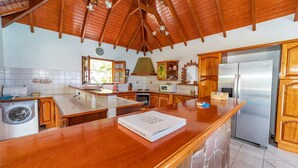 Una cocina con armarios de madera, un refrigerador de acero inoxidable, una lavadora y una isla grande con un libro titulado "SAINT-BARTH GUEST BOOK".