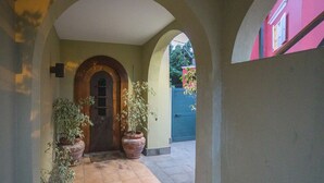 Um corredor com chão de azulejos, porta de madeira e plantas em vasos.