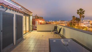 Terraço no telhado com mesa e cadeiras, vista da paisagem urbana e palmeiras.