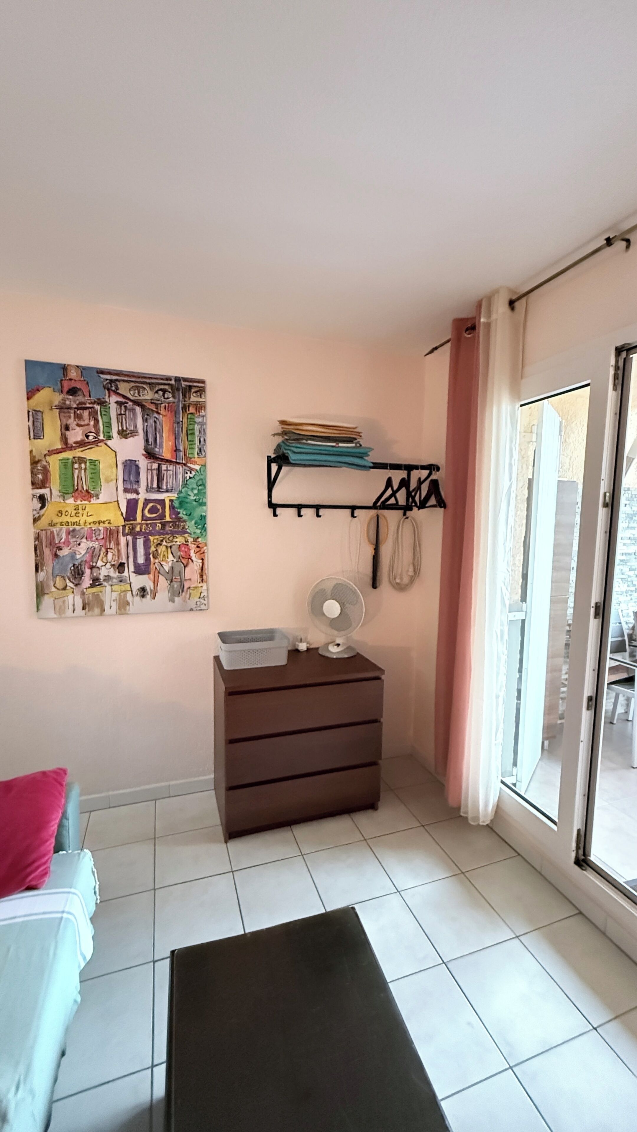 Ein Zimmer mit einem Bett, einem Schrank, einem Ventilator, einem Gemälde und einem Fenster mit Vorhängen.