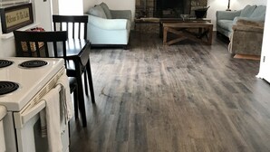 A modern kitchen with a stove, dining table, and chairs. There is a stone fireplace with a TV mounted above it. - Secluded Lakehouse Right on Lake Eufaula! (Crowder)