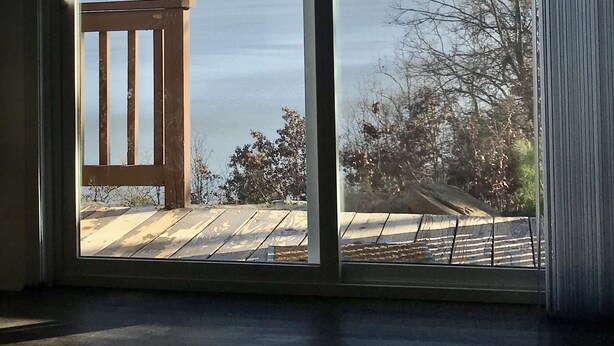 A room with a large sliding glass door leading to a deck overlooking a body of water. - Secluded Lakehouse Right on Lake Eufaula! (Crowder)