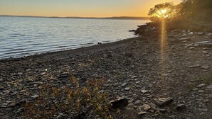 A rocky shoreline with a calm body of water and a sunset in the background. - Secluded Lakehouse Right on Lake Eufaula! (Crowder)
