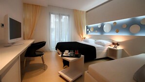 A modern hotel room with a bed, a desk with a computer, a chair, and a bedside table with a lamp. - Domador Rooms & Apartments (Becici)