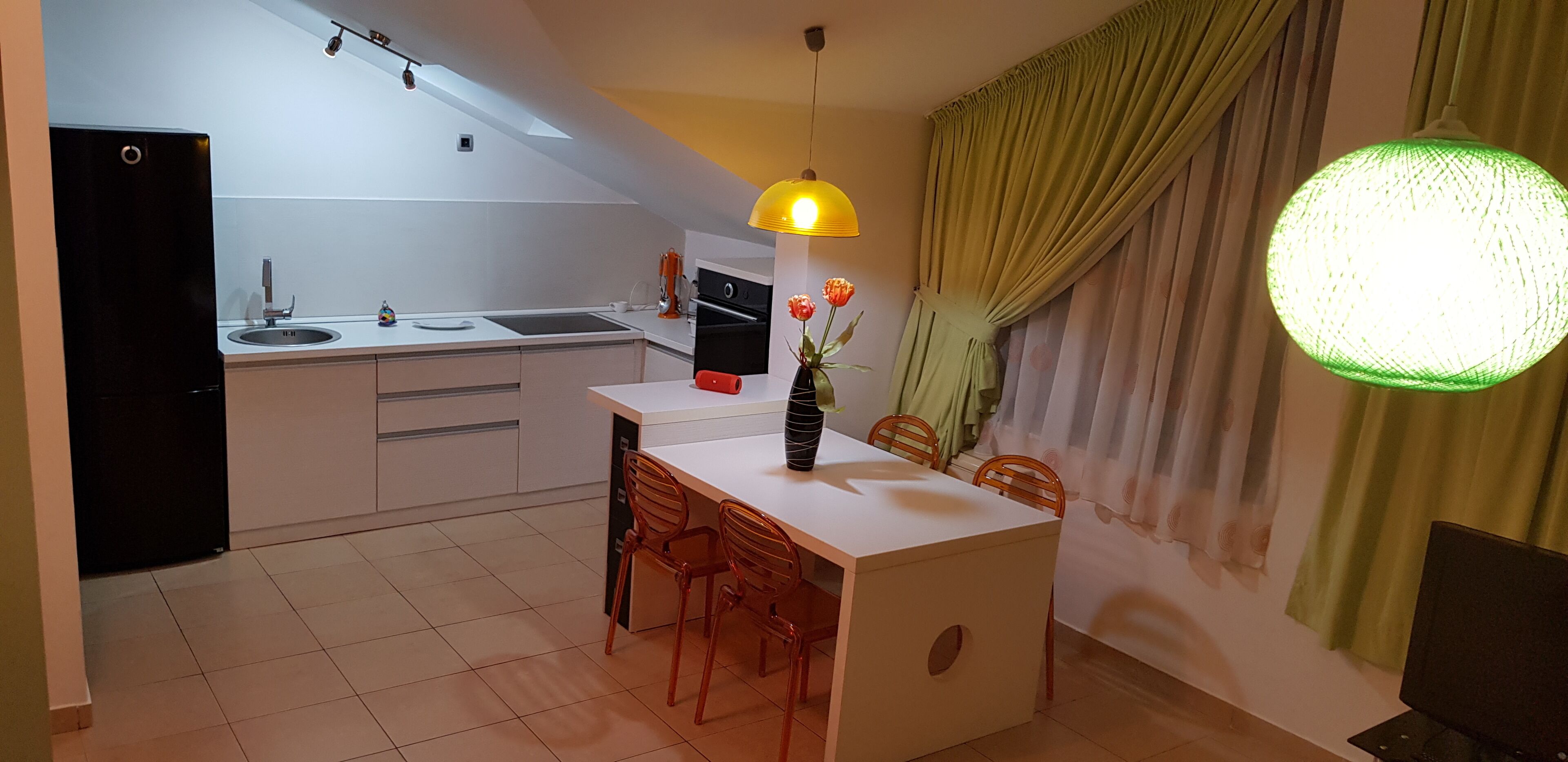 A compact kitchen with a white countertop, a black refrigerator, a sink, and a dining area with two chairs.