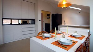 A modern dining area with a white table set for four, orange placemats, and a pendant light above. - Domador Rooms & Apartments (Becici)