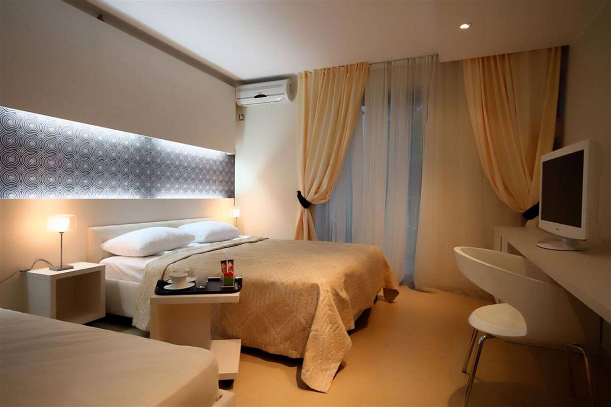 Une chambre d’hôtel comprenant un lit, une table de chevet avec une lampe, un bureau avec une chaise, une télévision et des rideaux.