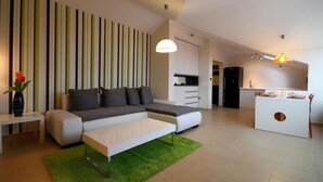 A modern living room with a sectional sofa, a coffee table, and a kitchen area with a dining table. - Domador Rooms & Apartments (Becici)