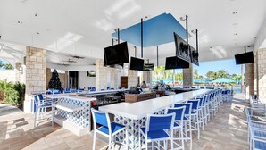 An outdoor bar area with a long counter, multiple TVs, and blue chairs. - PROMO Elegant 9 BR Villa, Pool/Spa, Resort - by Blue Sky Villas (Davenport)