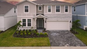 A two-story house with a garage, a front porch, and a well-maintained lawn. - PROMO Elegant 9 BR Villa, Pool/Spa, Resort - by Blue Sky Villas (Davenport)