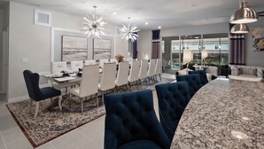 A modern dining area with a large table, white chairs, and a blue sofa. - PROMO Elegant 9 BR Villa, Pool/Spa, Resort - by Blue Sky Villas (Davenport)