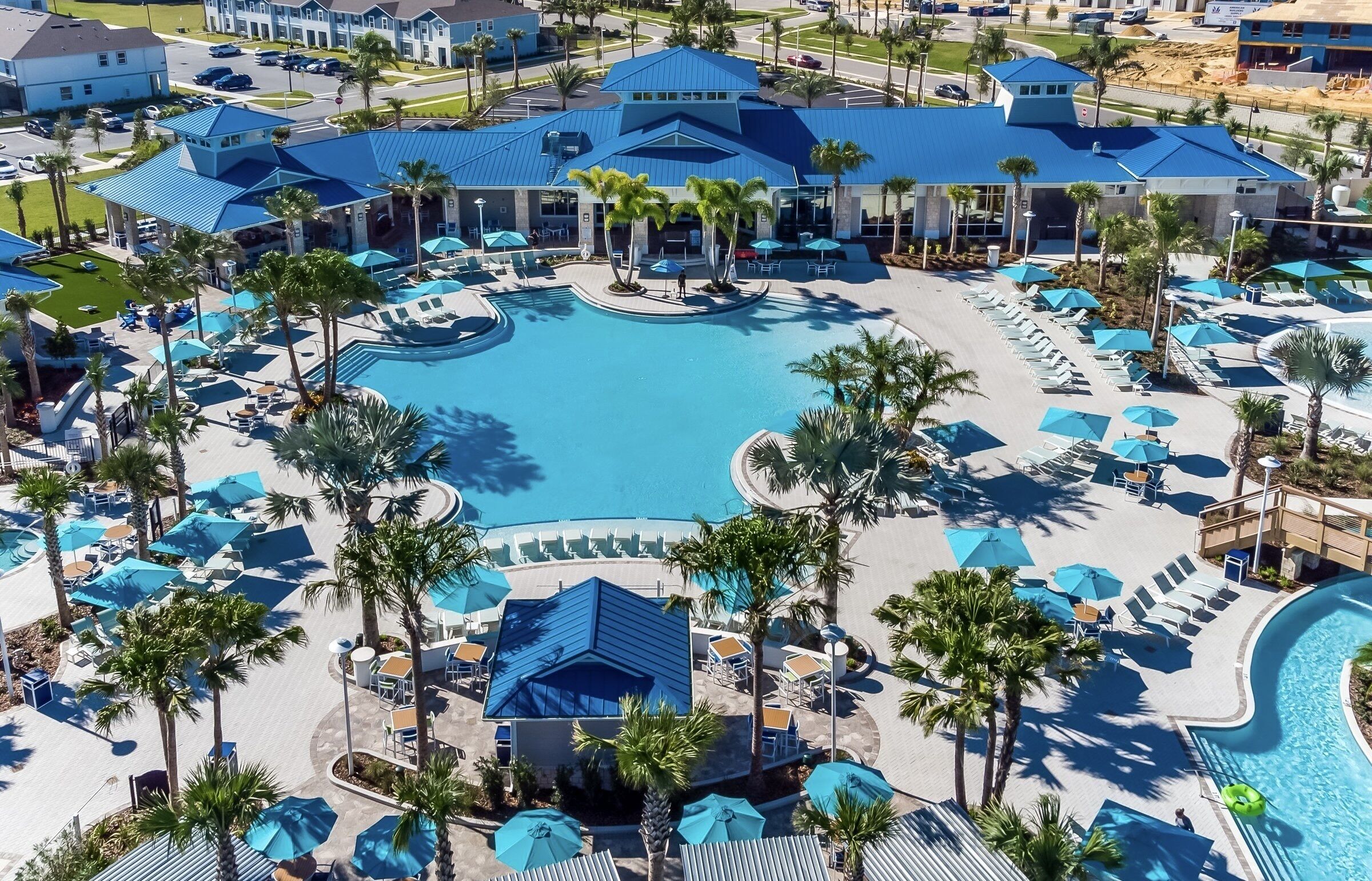 Un resort con una amplia piscina central, varias zonas de descanso con sombrillas y palmeras.