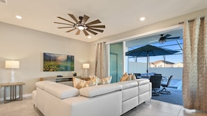 Un salón amplio con un sofá blanco grande, un ventilador de techo y vistas al patio exterior.
