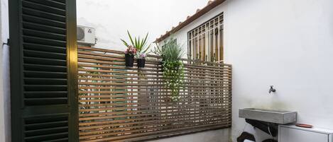 A wooden fence with potted plants, a concrete sink, and a white cabinet in a courtyard.