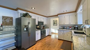 A modern kitchen with white cabinets, stainless steel appliances, and wooden flooring. - RIVER PARK HOME with GARAGE & EV CHARGER, Spa, Home Theatre + Arcade, 3,000 SqFt (Spokane)