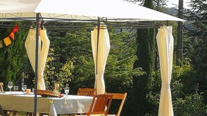 Een buitenmeedeel met een tafel en stoelen onder een overkapping, omgeven door groen.