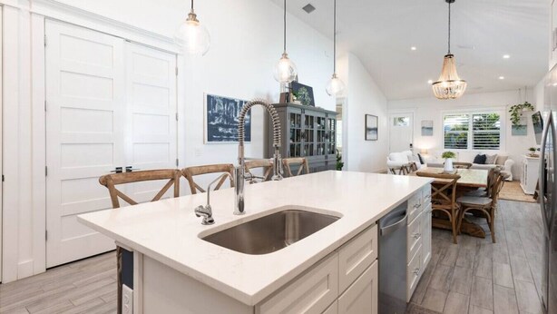 A modern kitchen with a central island, pendant lighting, and a dining area with wooden chairs and a white table. - 3 BR Luxury, Anna Maria Island, IMG (Bradenton)