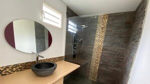 Een moderne badkamer met een stenen wastafel, een grote spiegel en een douchecabine met glazen wanden.