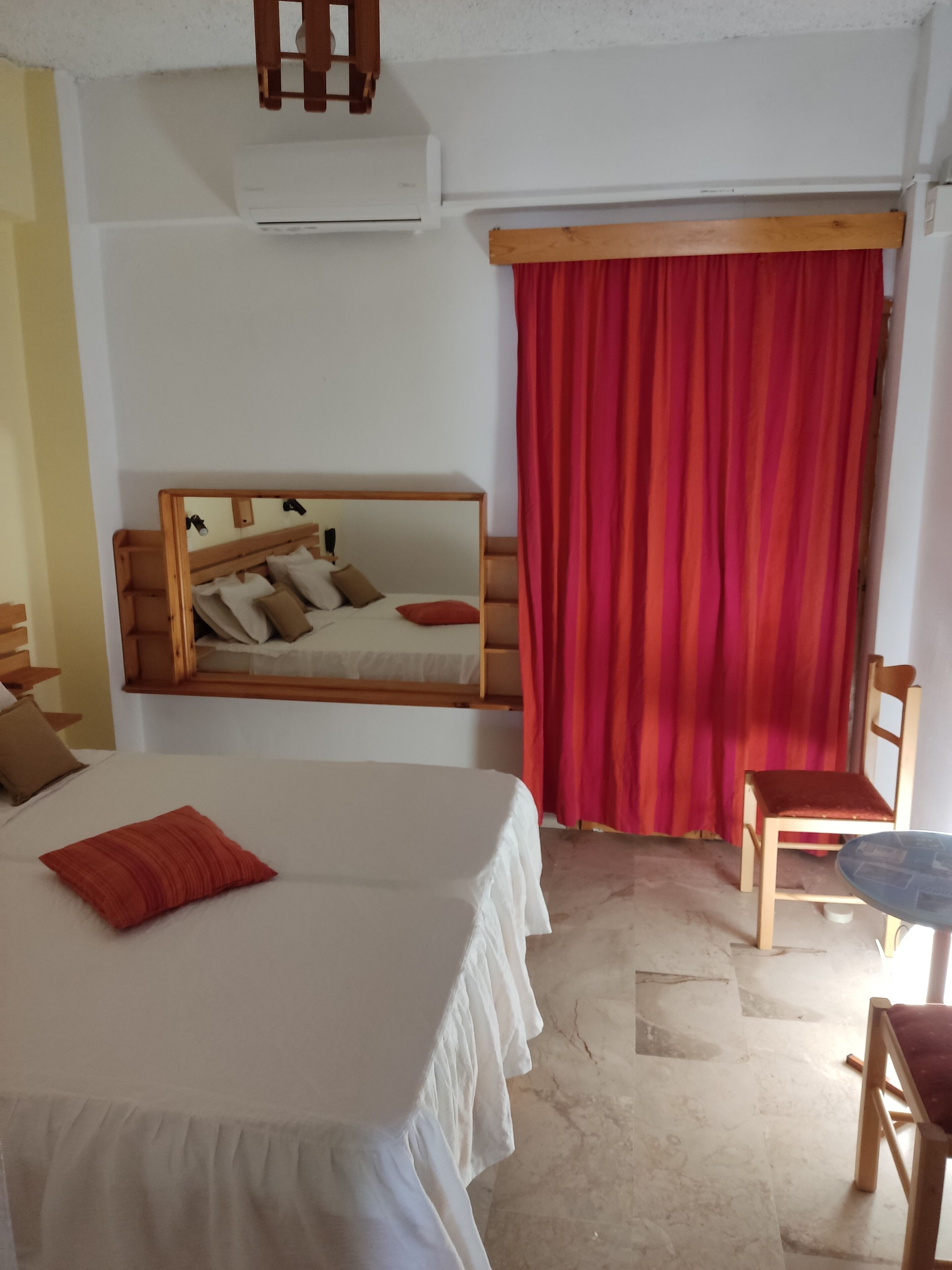Un dormitorio con una cama, una silla, una mesa y una ventana con cortinas rojas.