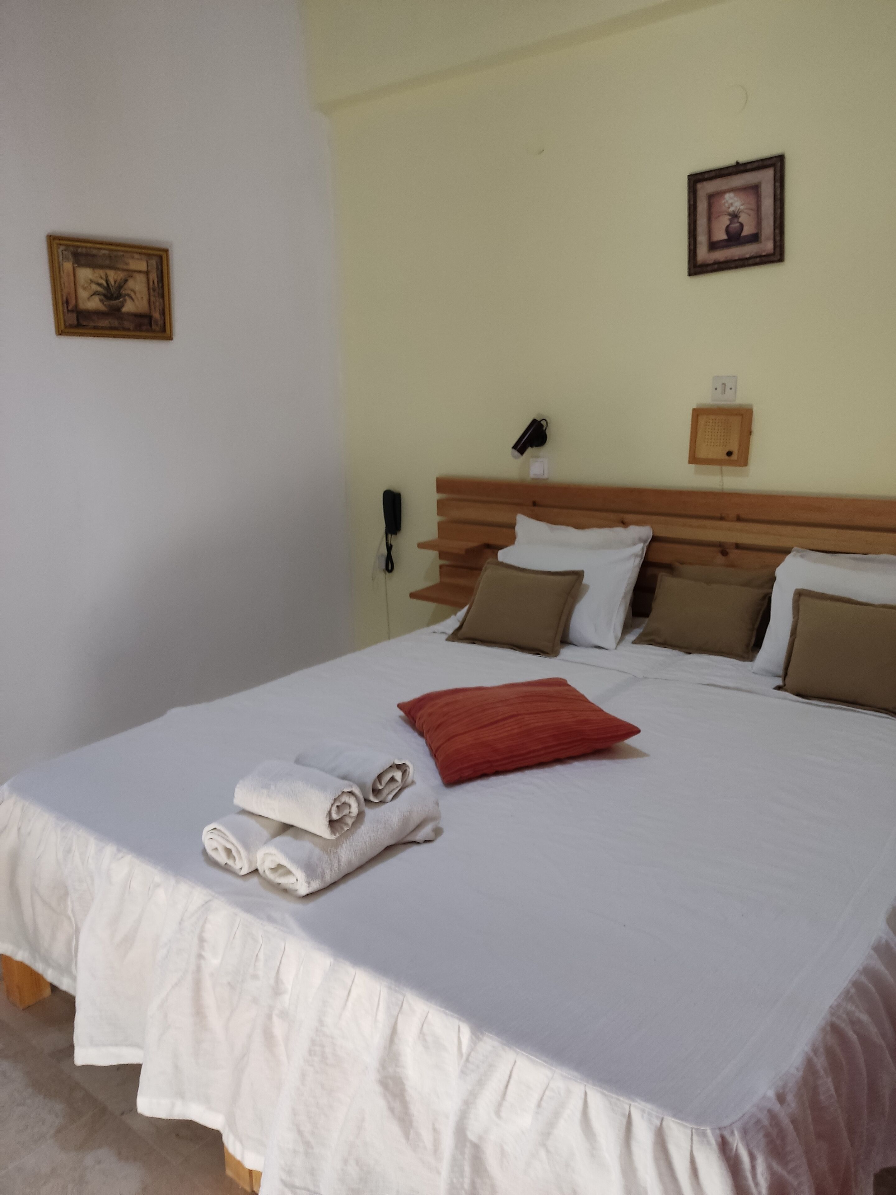 Una cama bien hecha con sábanas blancas, una almohada roja y toallas enrolladas al lado.
