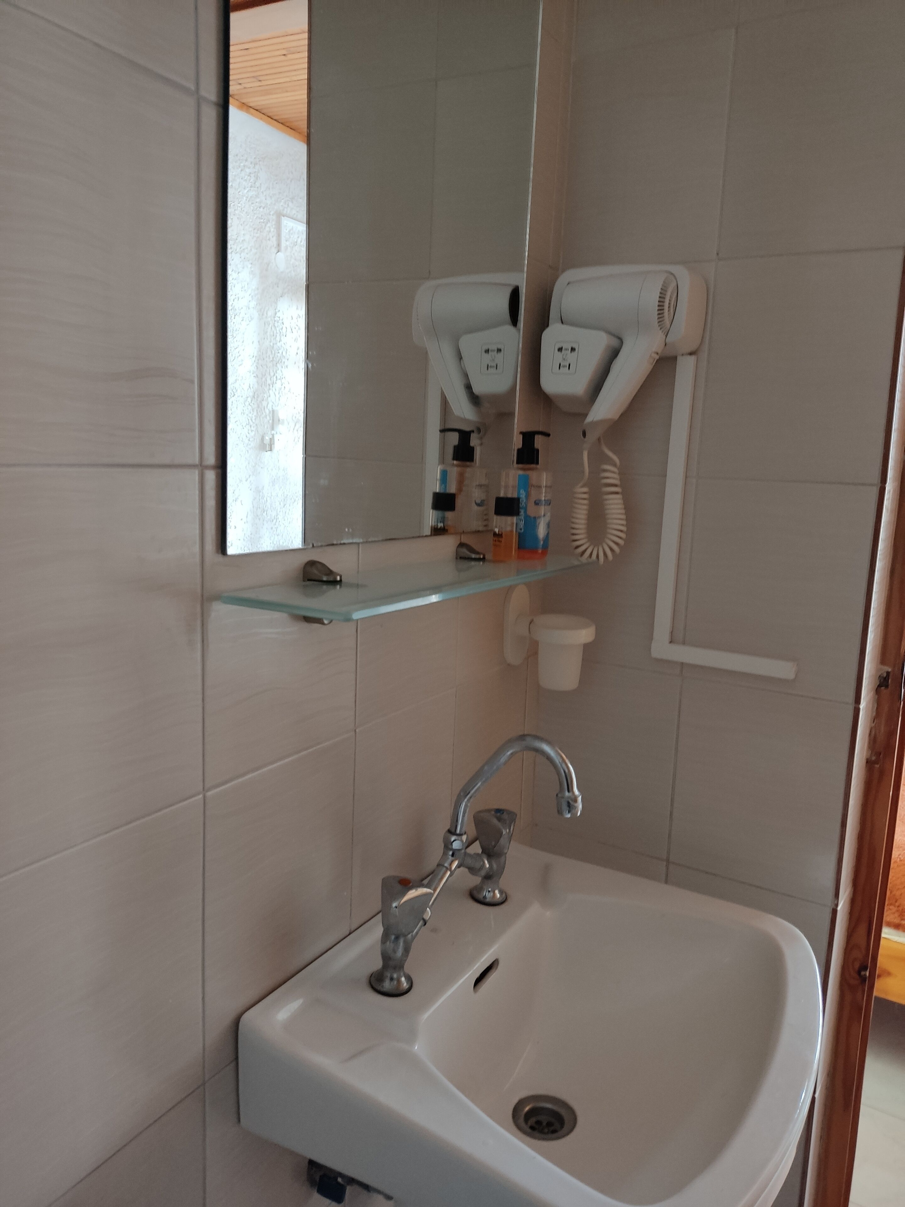 A bathroom with a white sink, a mirror, and two hair dryers mounted on the wall.