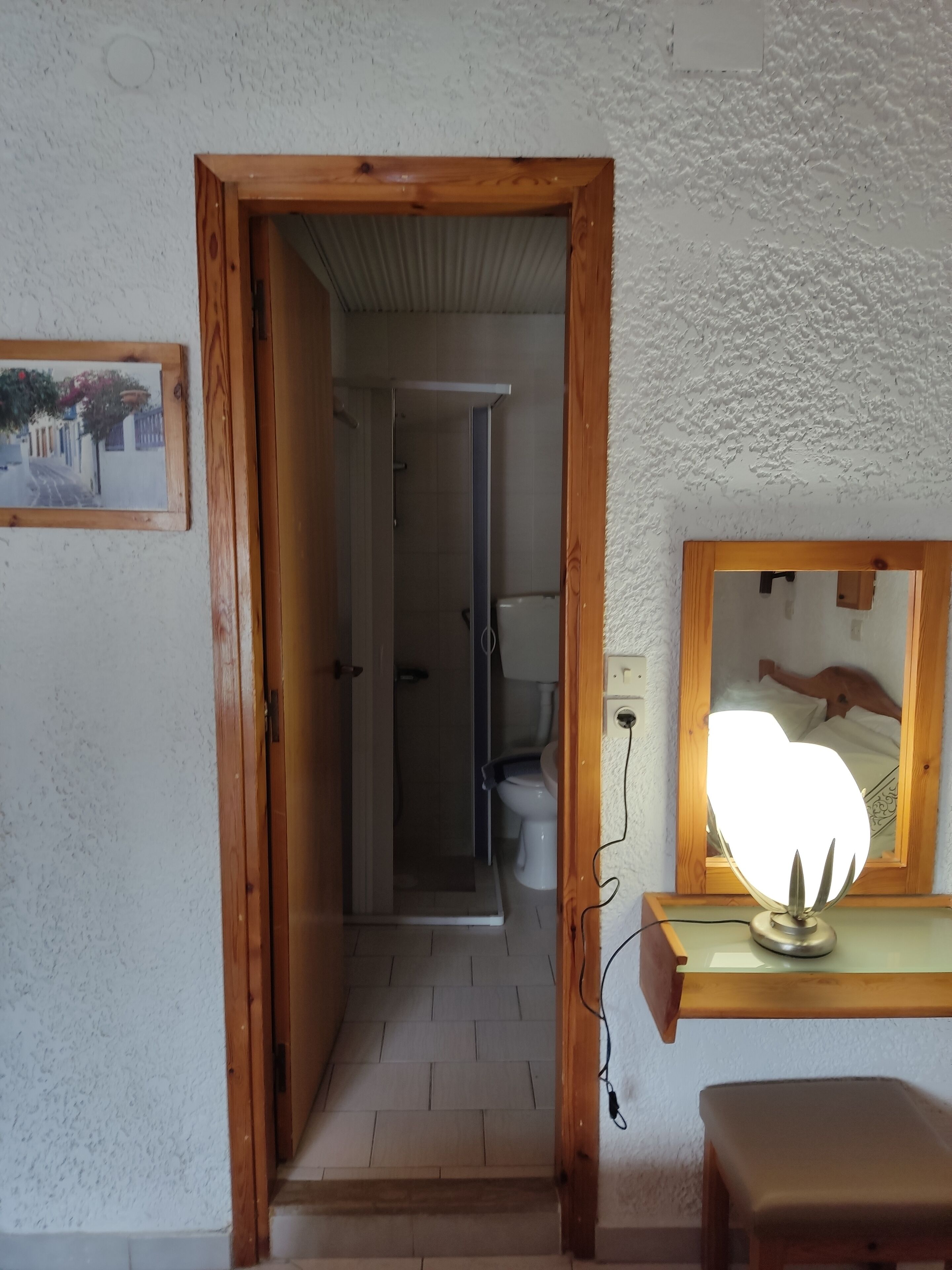 Un corridoio stretto con una porta in legno che conduce al bagno. A destra, uno specchio con un lampadario è fissato alla parete.
