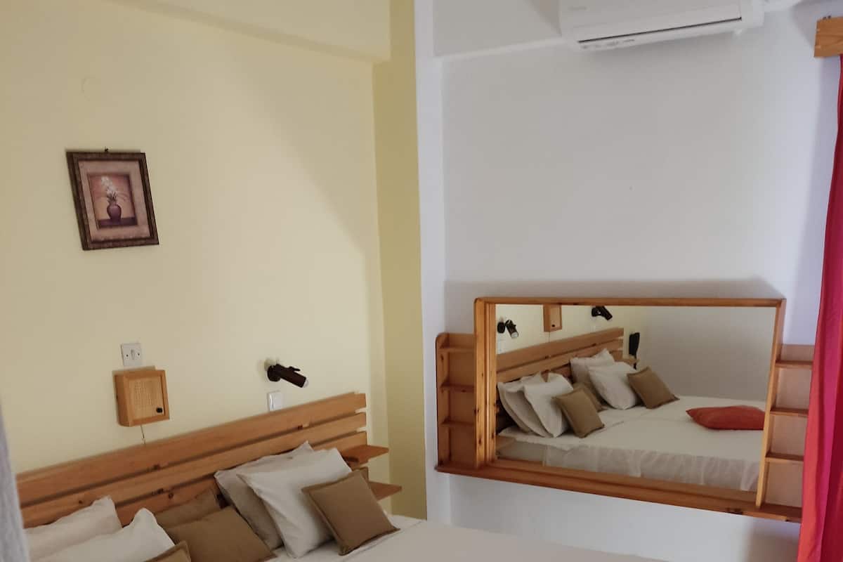 Habitación de hotel con una cama grande, una mesita de noche, un espejo y un aire acondicionado instalado en la pared.