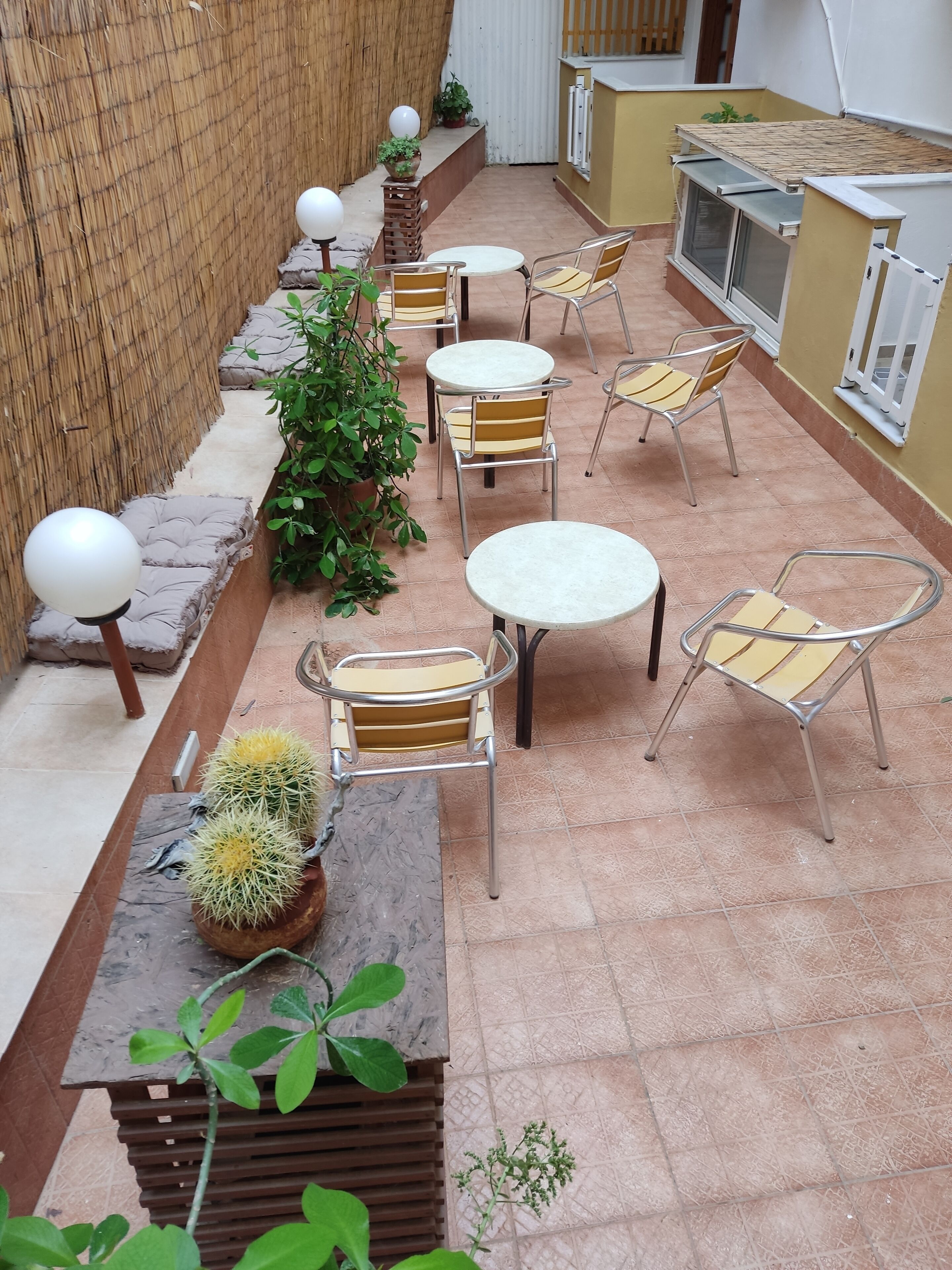 An outdoor patio area with round tables and chairs, potted plants, and a wooden bench.