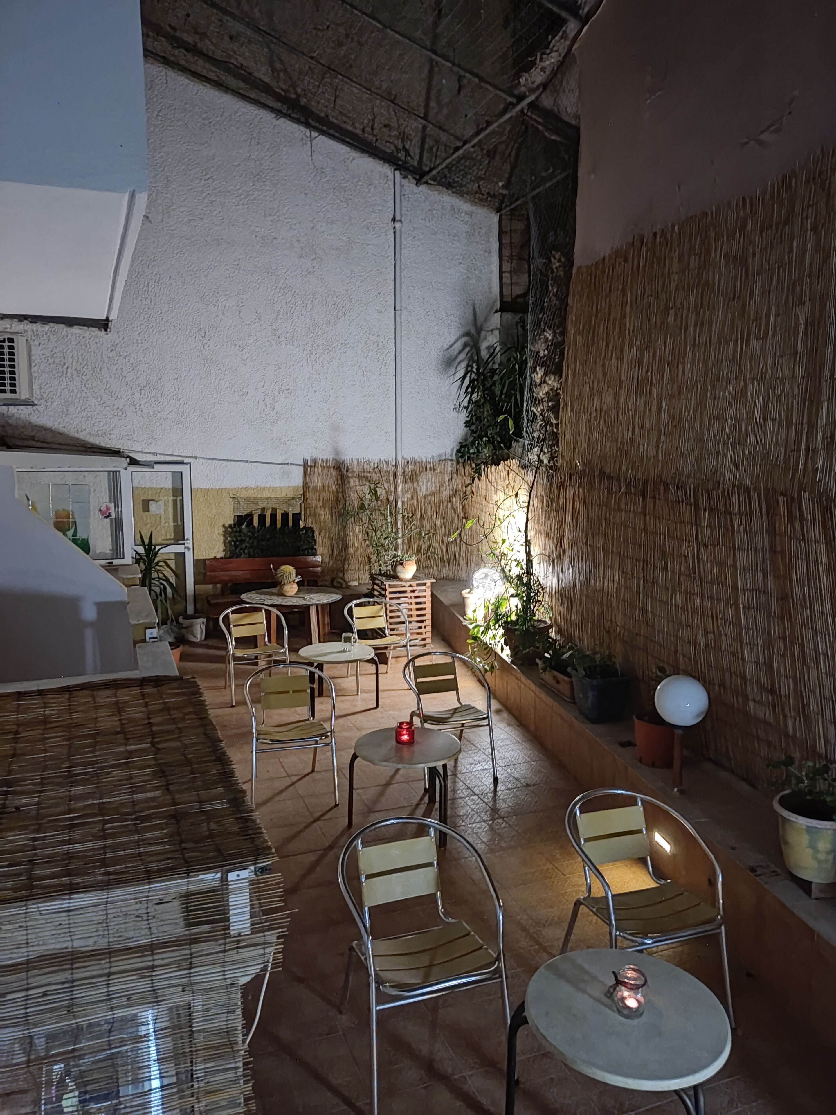 An indoor patio area with metal chairs and tables, a thatched wall, and potted plants.