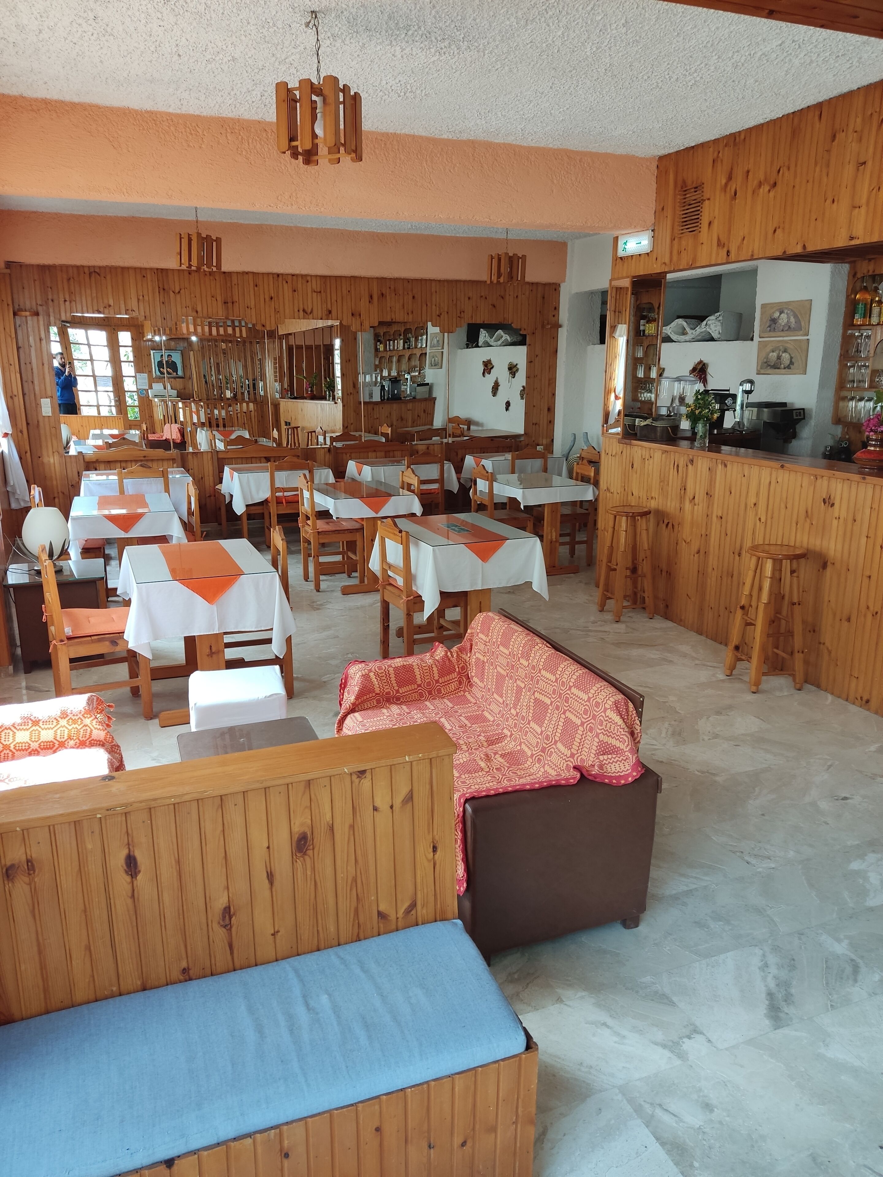A restaurant with wooden interiors, tables with white and orange tablecloths, and a bar area.