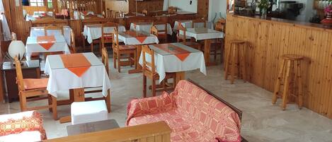 A restaurant with wooden interiors, tables with white and orange tablecloths, and a bar area.