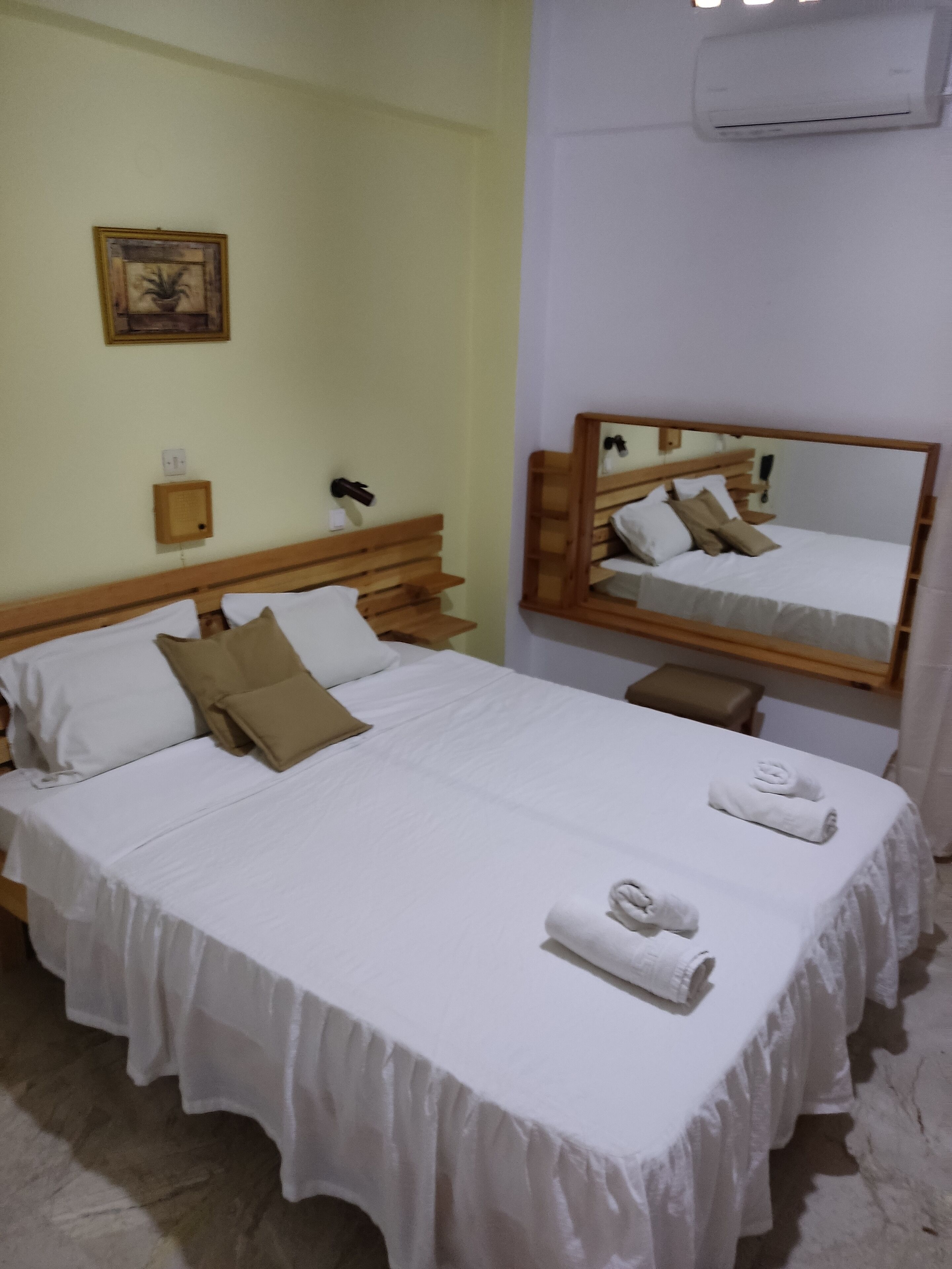 Una cama bien hecha con sábanas blancas, un cabecero de madera y una mesita de noche con una lámpara.