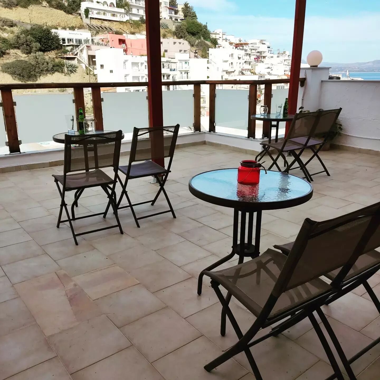 A terrace with a round table and chairs, a red candle, and a view of a coastal town.