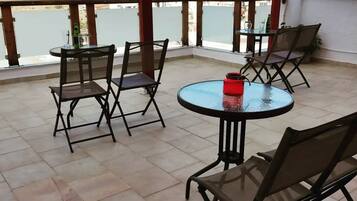 A terrace with a round table and chairs, a red candle, and a view of a coastal town.